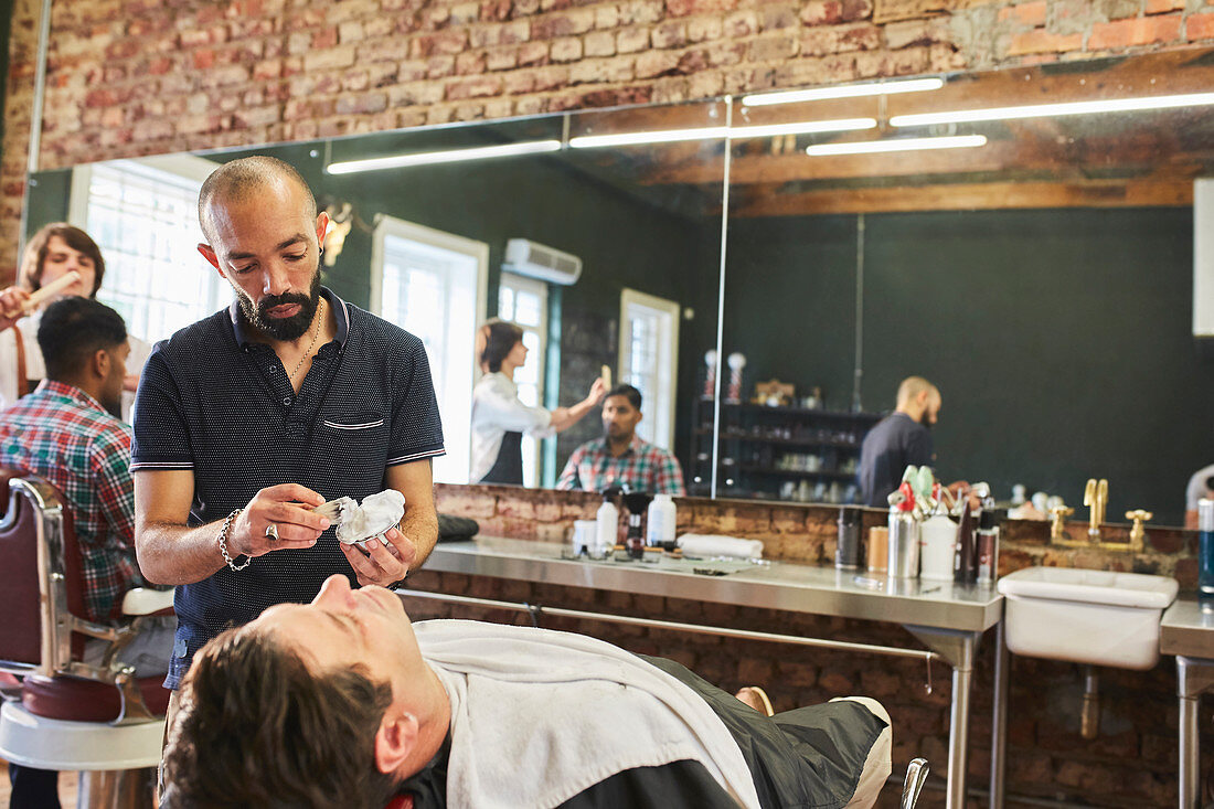Male barber preparing to shave face of customer