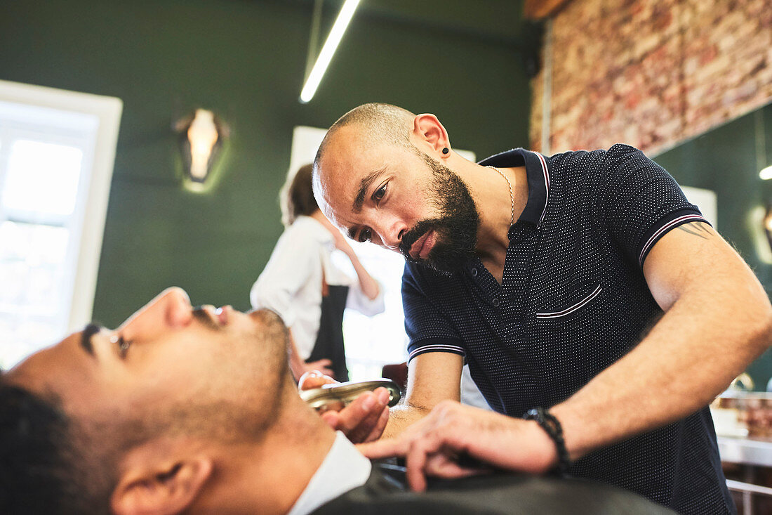 Focused male barber giving customer a shave