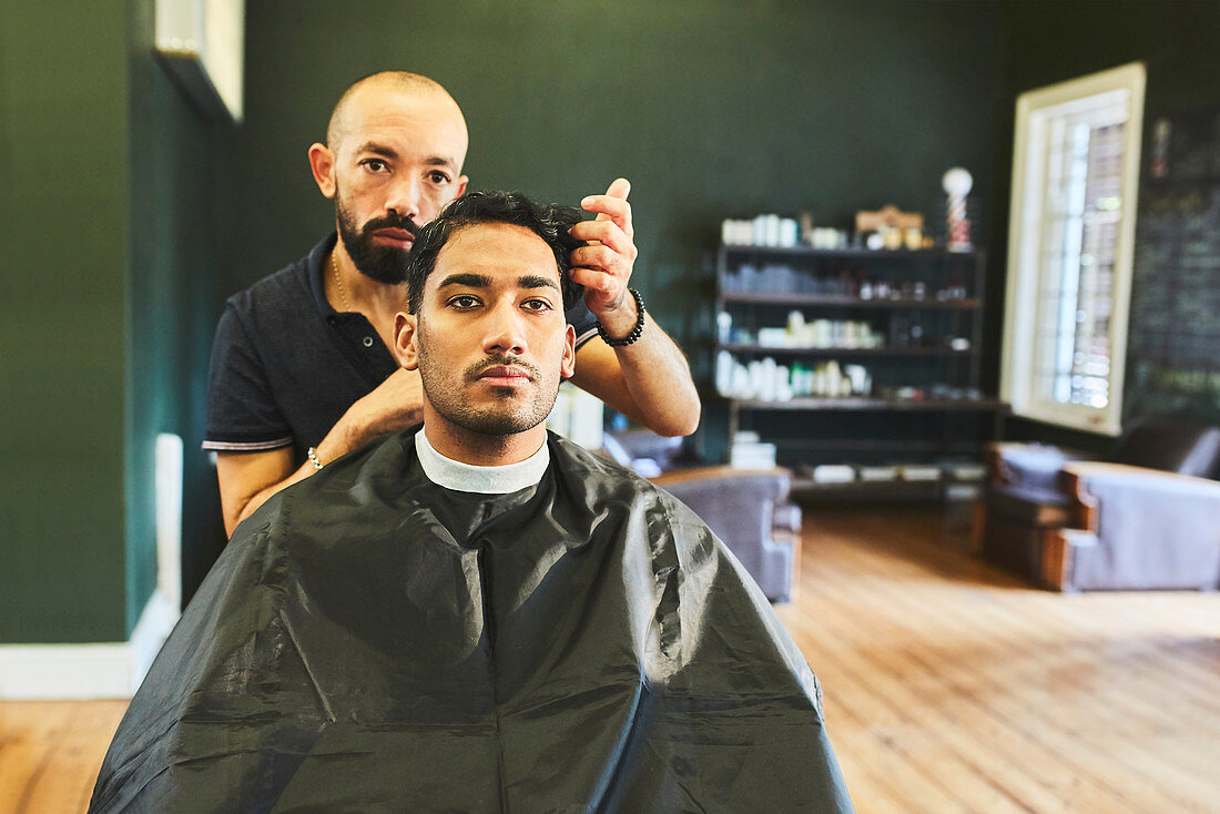 Male barber giving customer haircut in barbershop