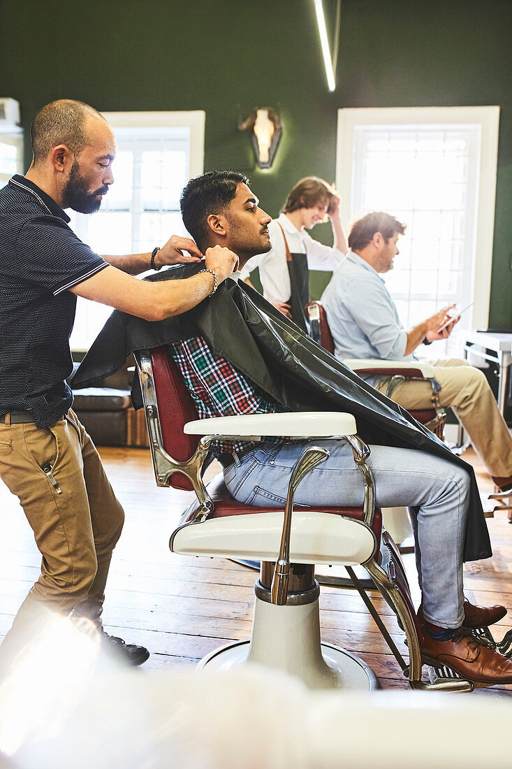 Male barber preparing customer for haircut