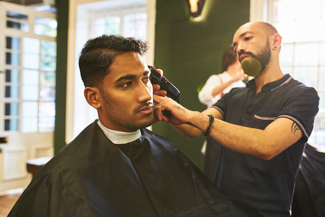 Male barber shaving hair of customer in barbershop