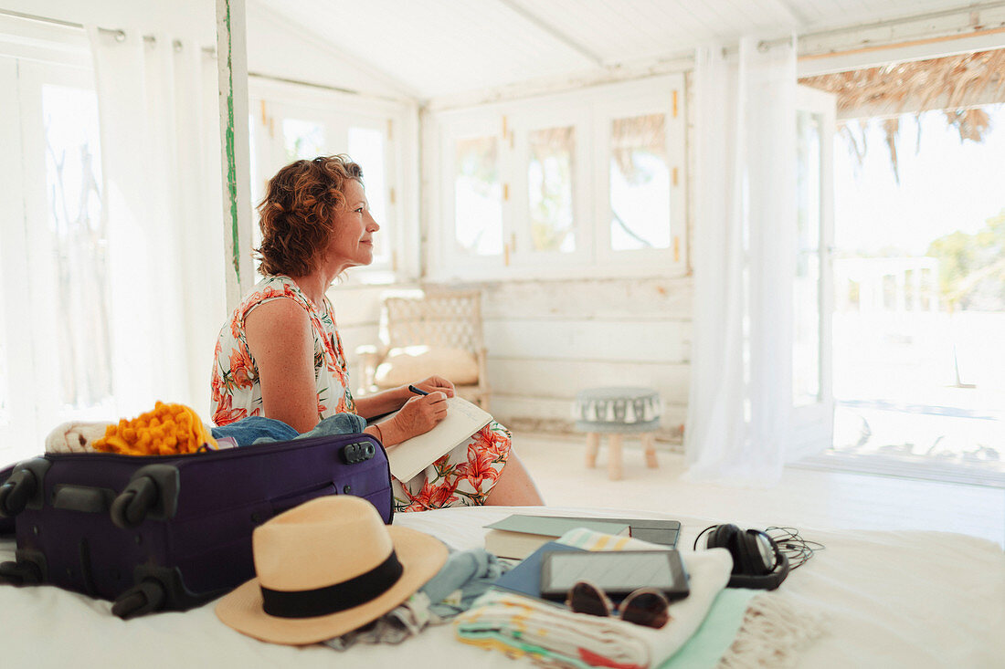 Serene woman writing in journal next to suitcase