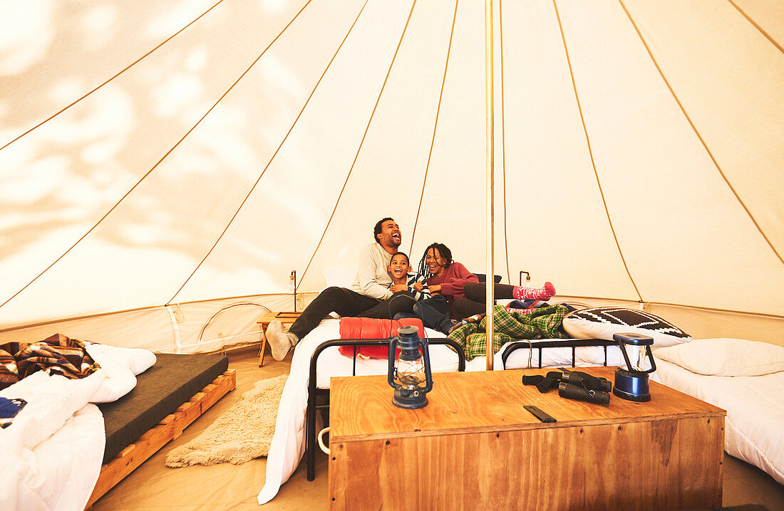 Happy, carefree family relaxing on bed in camping yurt