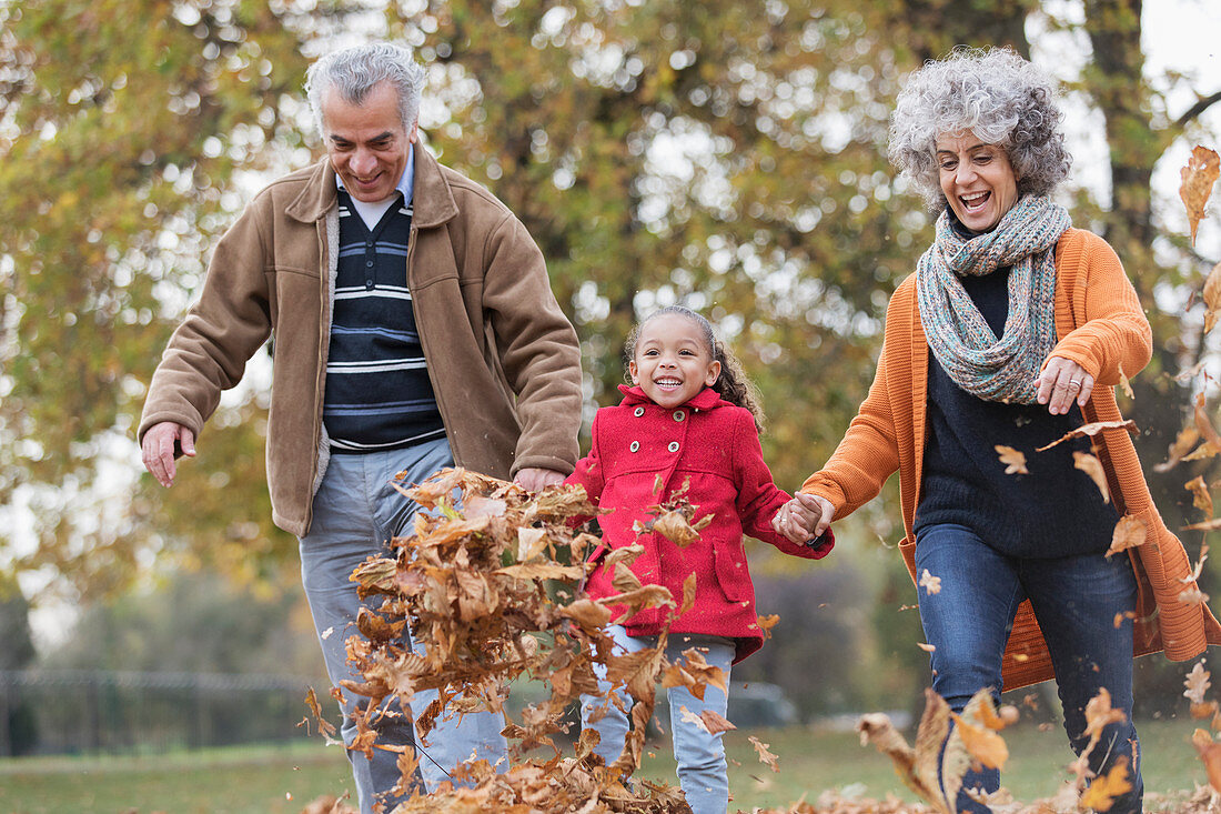 Grandparents and granddaughter kicking autumn leaves