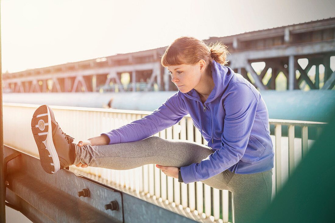 Young female runner stretching leg on urban railing