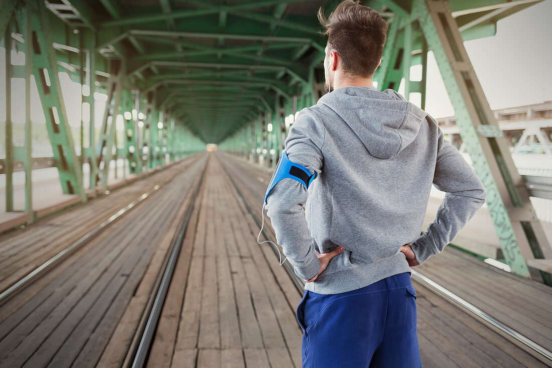 Young male runner standing on train tracks