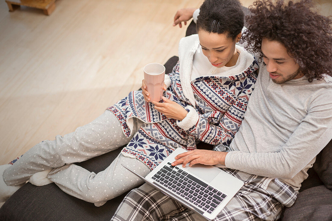 Couple in pyjamas relaxing, using laptop on sofa