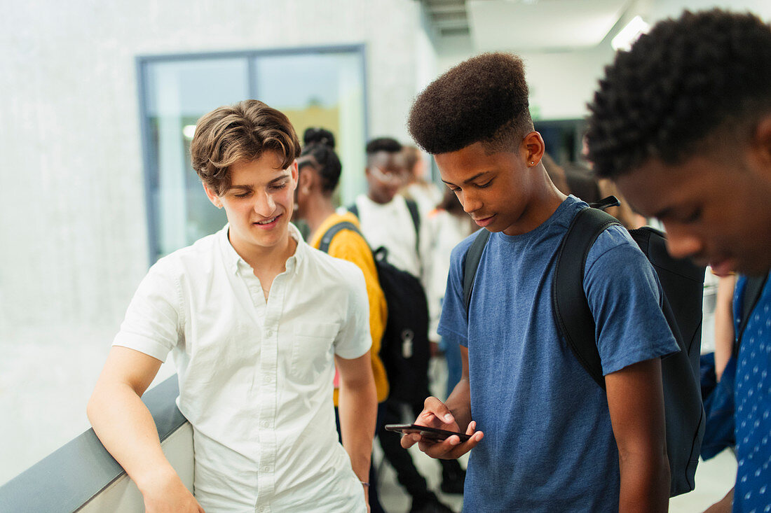 Junior high boy students using smart phone in corridor