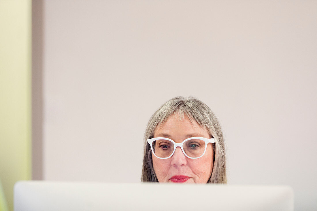 Focused mature woman in eyeglasses using computer