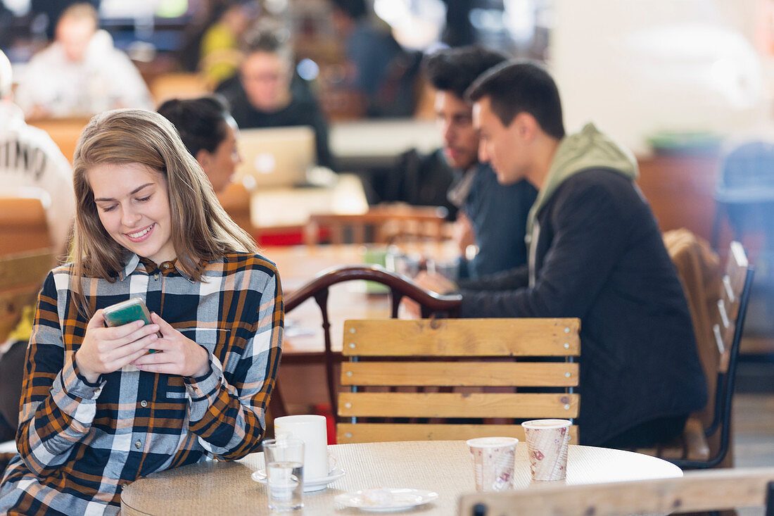 Smiling young woman using smart phone in cafe