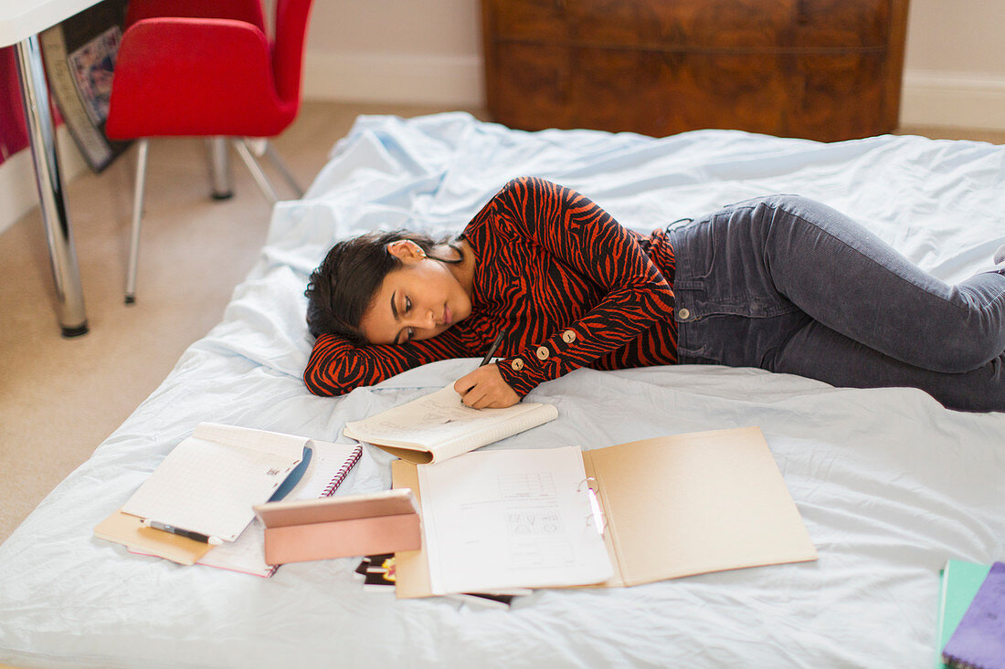 Teenage girl doing homework laying on bed