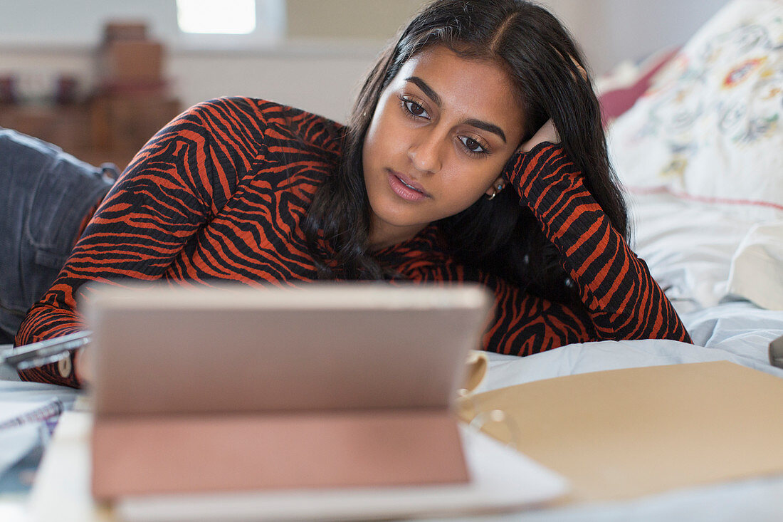Focused teenage girl studying at digital tablet on bed