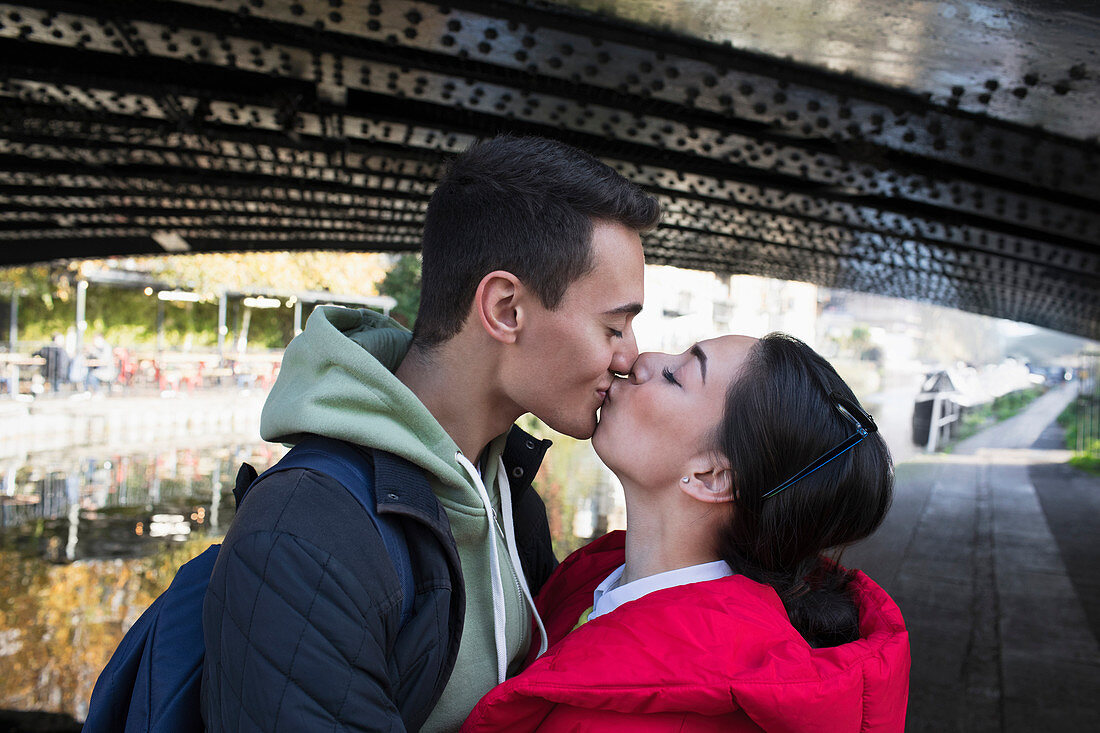 Affectionate young couple kissing under bridge