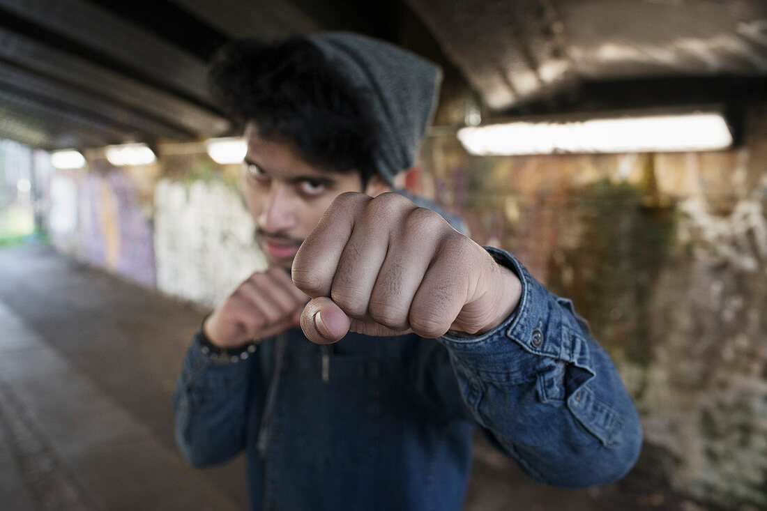 Portrait tough young man punching in urban tunnel