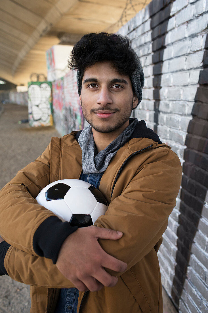 Portrait young man with soccer ball in urban tunnel