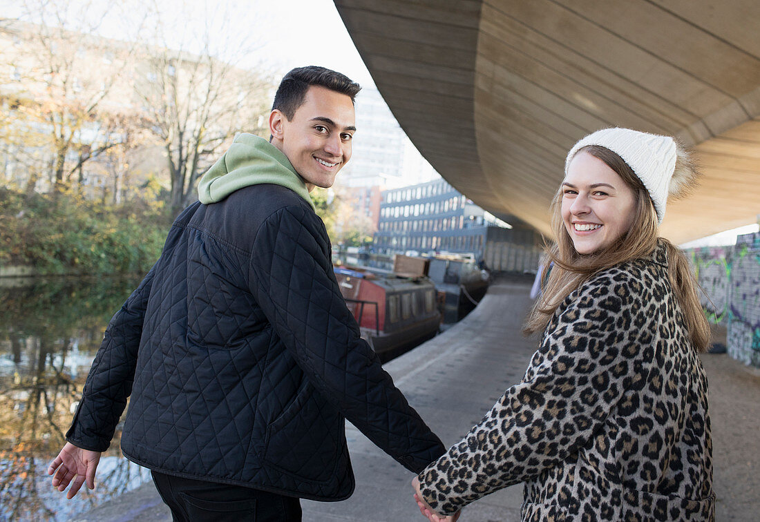 Portrait happy couple holding hands, walking along canal