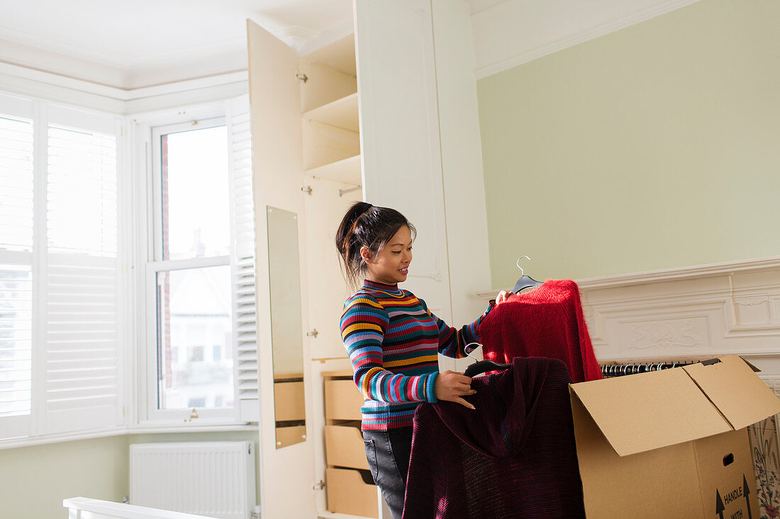 Woman unpacking clothing from moving box in bedroom