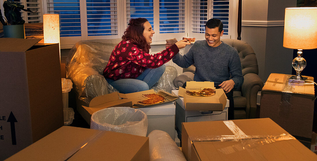 Happy couple taking a break from moving, eating pizza