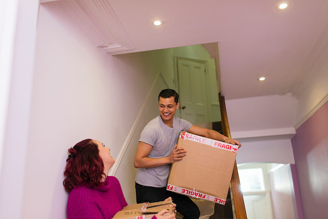 Couple moving house, carrying cardboard boxes on stairs