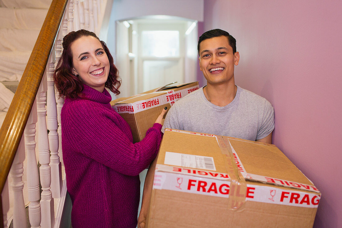 Couple moving house, carrying cardboard boxes in corridor