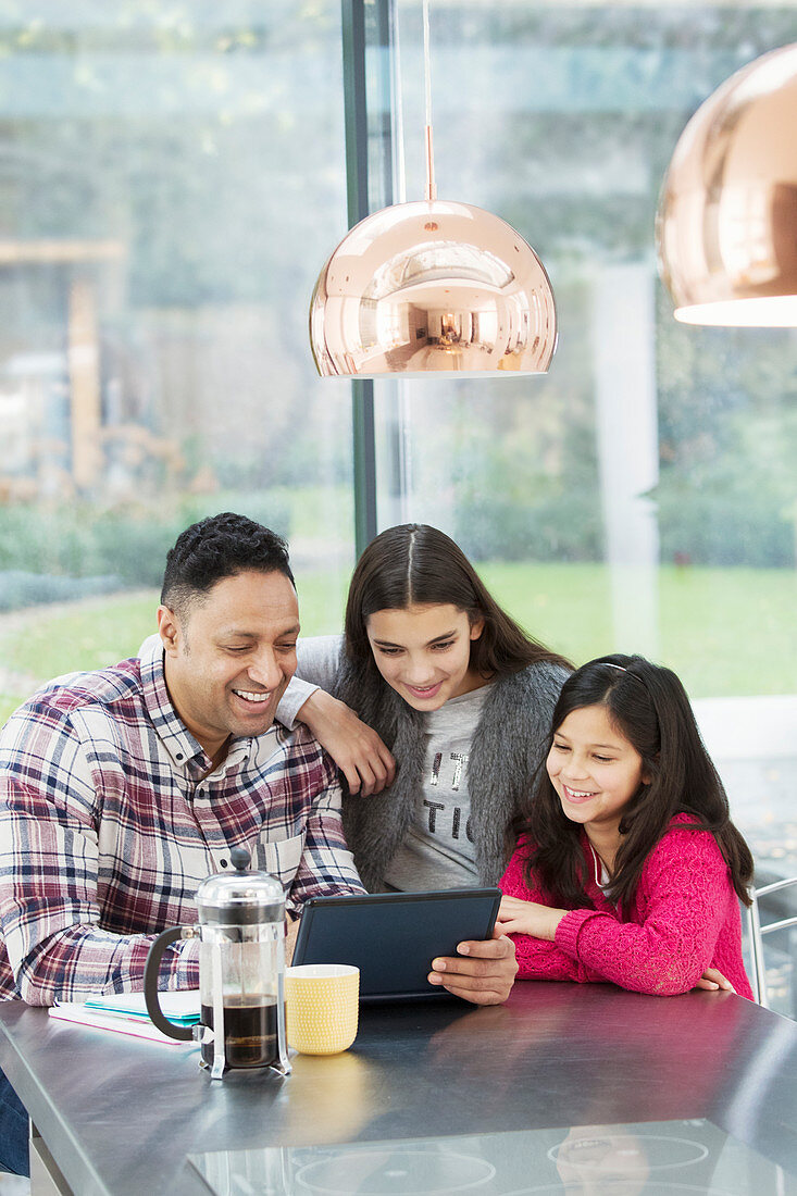 Happy father and daughters using tablet in morning kitchen