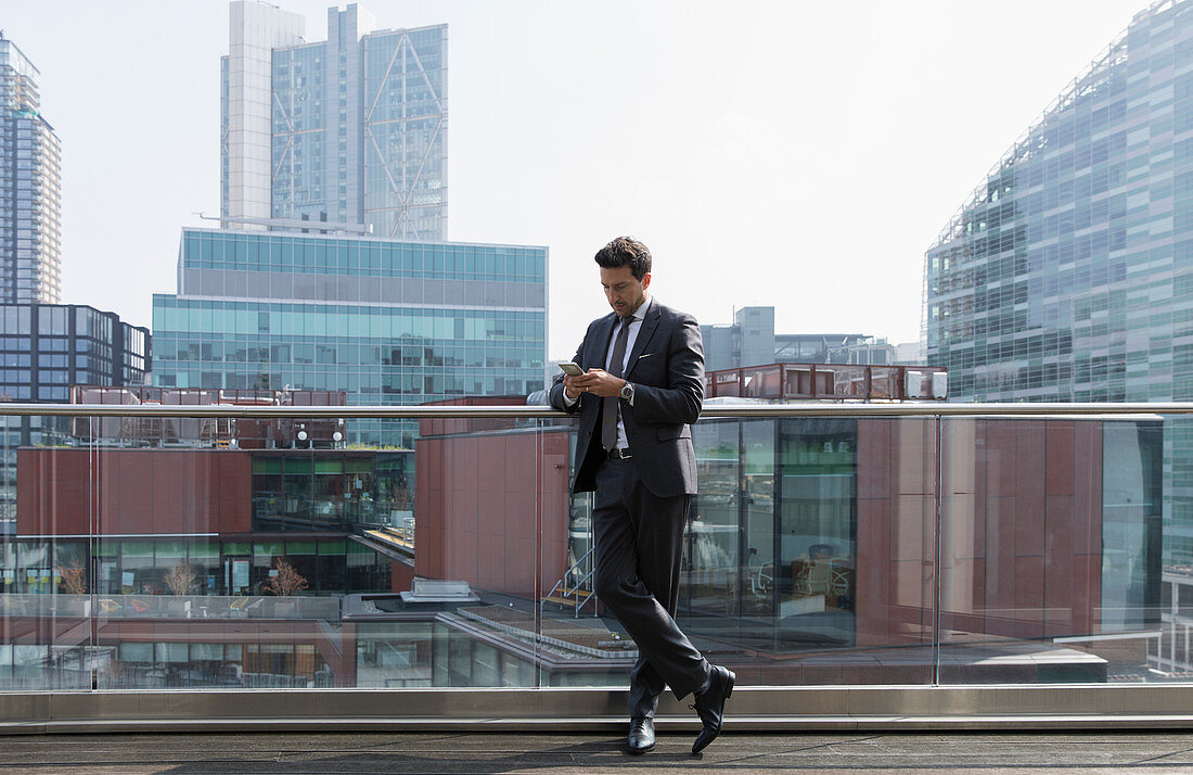 Businessman using smart phone on sunny urban balcony