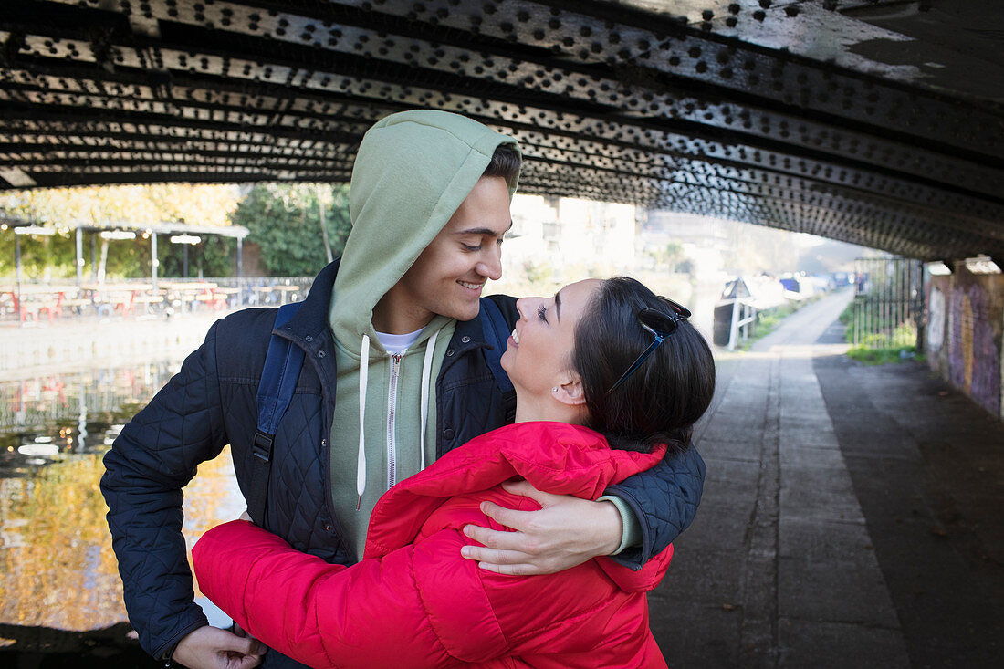 Happy, young couple hugging under urban bridge