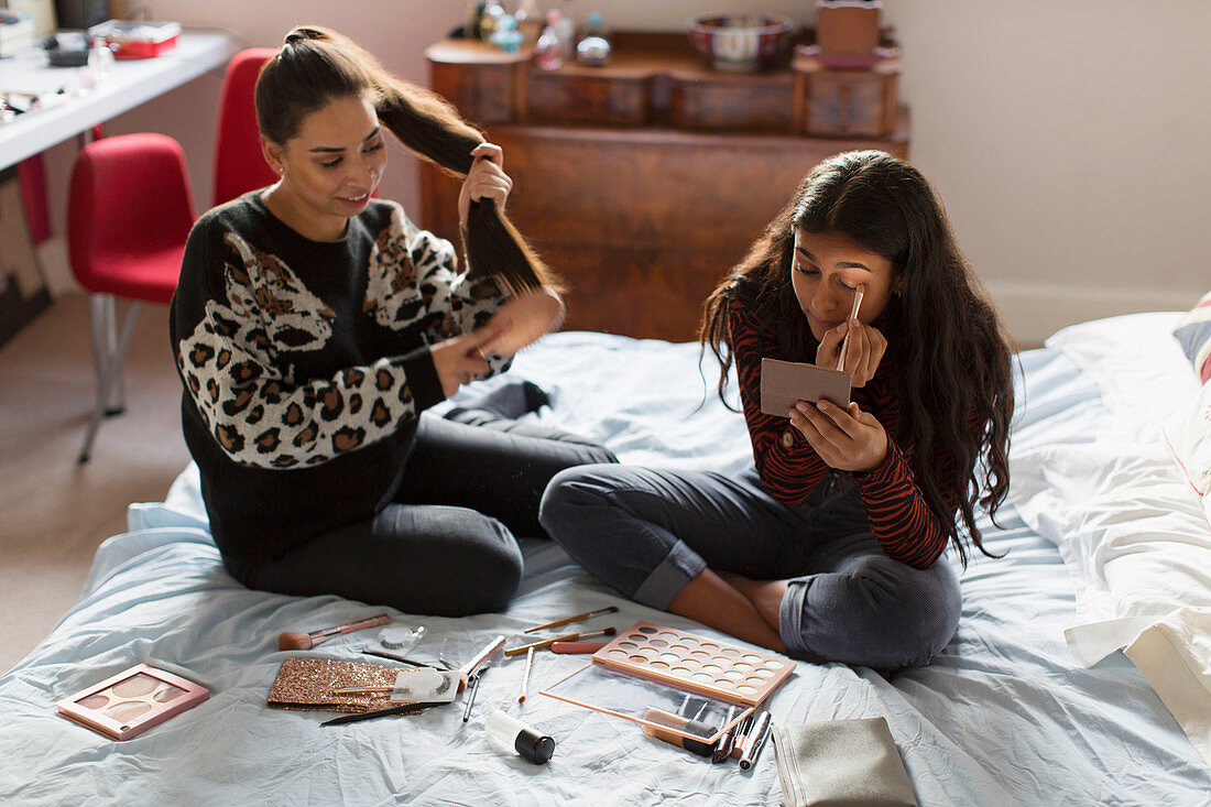Teenage girls applying makeup and brushing hair on bed