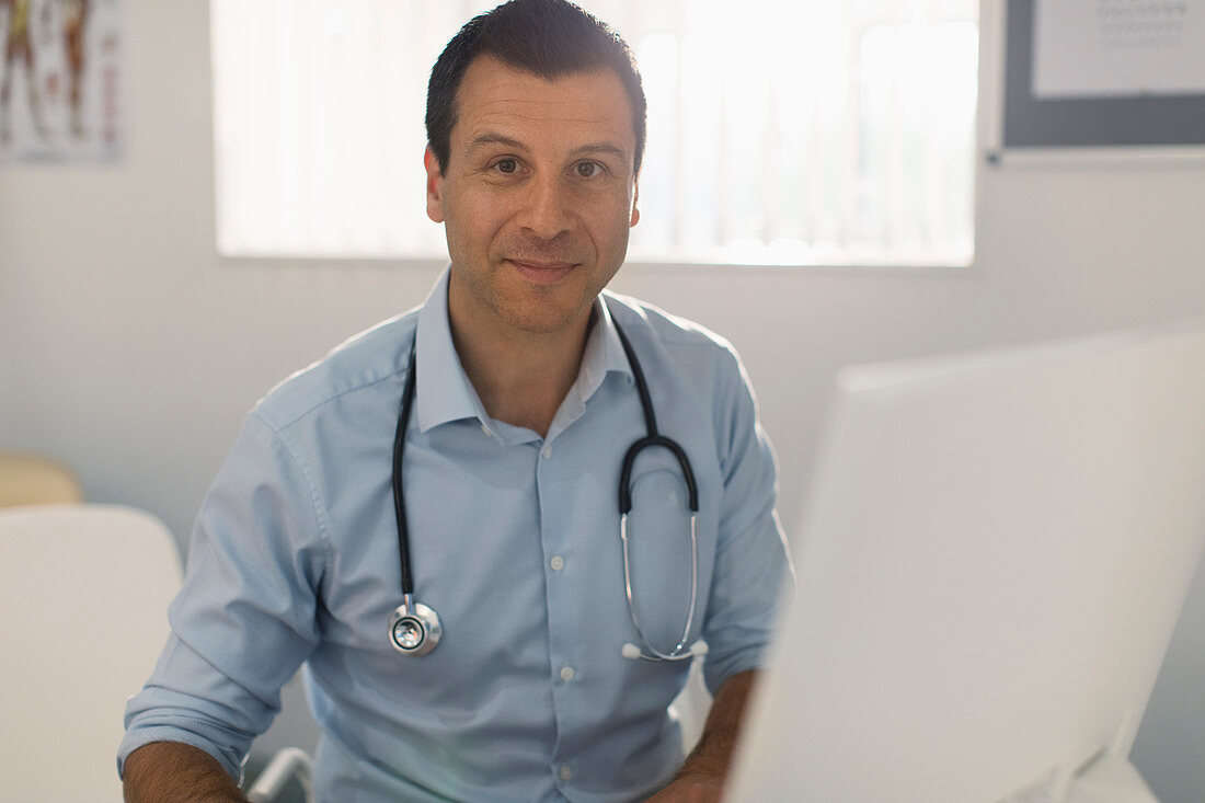 Portrait male doctor working at computer in doctors office