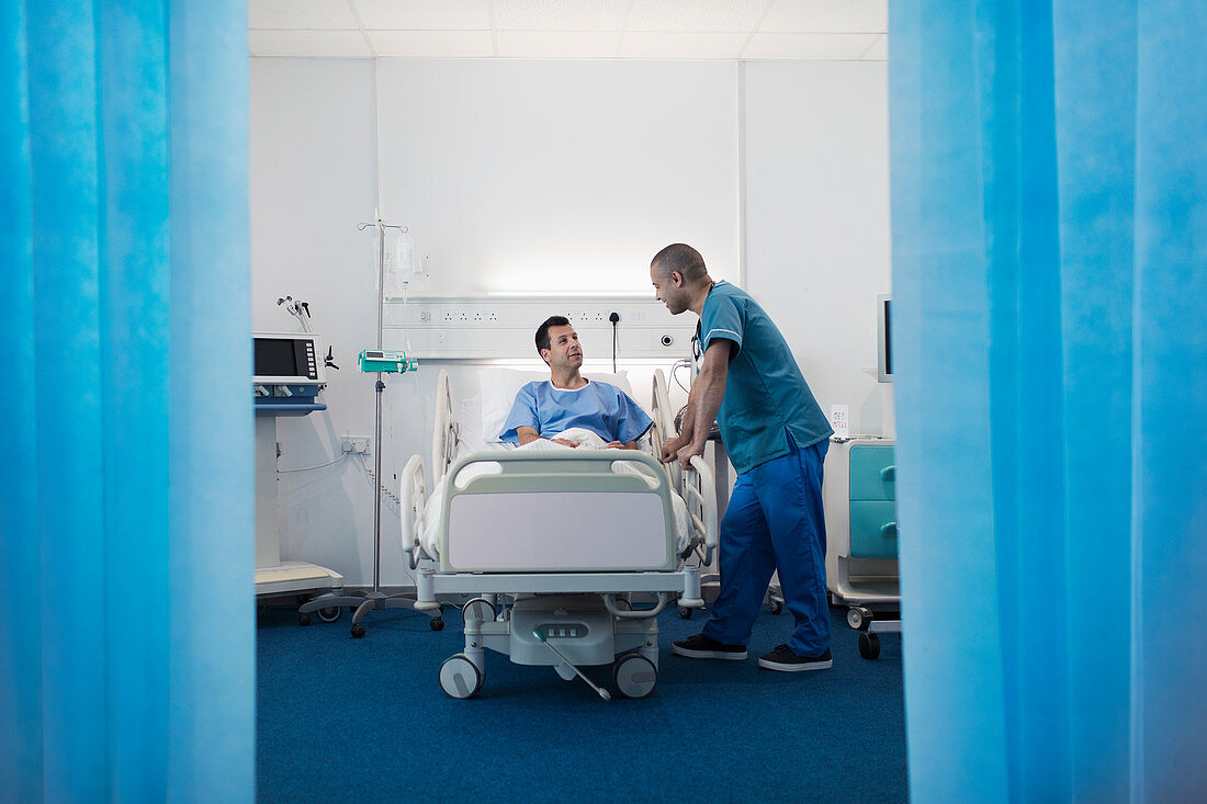 Male nurse talking with patient resting in hospital room