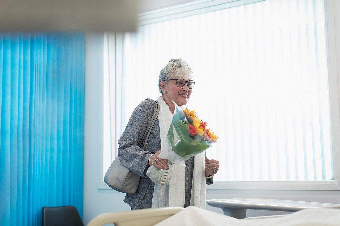 Senior visitor with flower bouquet in hospital room
