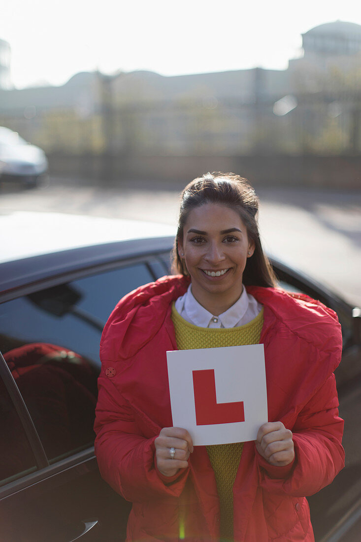 Portrait happy woman holding learner permit next to car