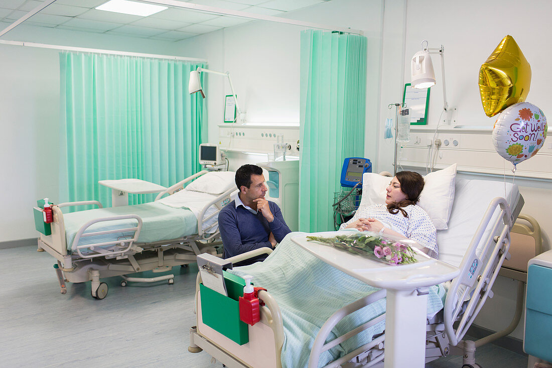 Man visiting, talking with wife resting in hospital ward