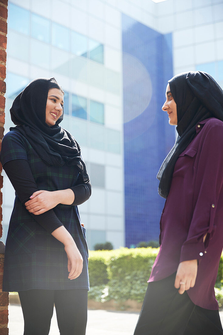 Women friends in hijabs talking outside sunny building