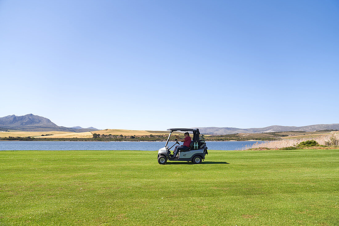 Male golfer driving golf cart along lake