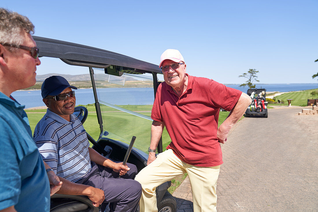 Happy golfer friends talking at golf cart on sunny course