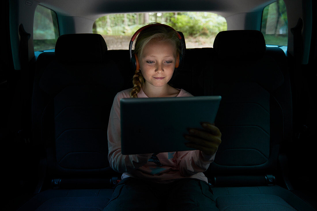 Girl with headphones and tablet in back seat of car