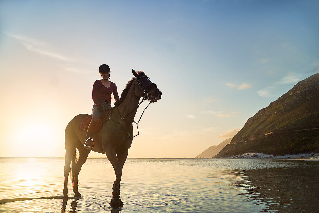 Woman horseback riding on tranquil sunset ocean beach