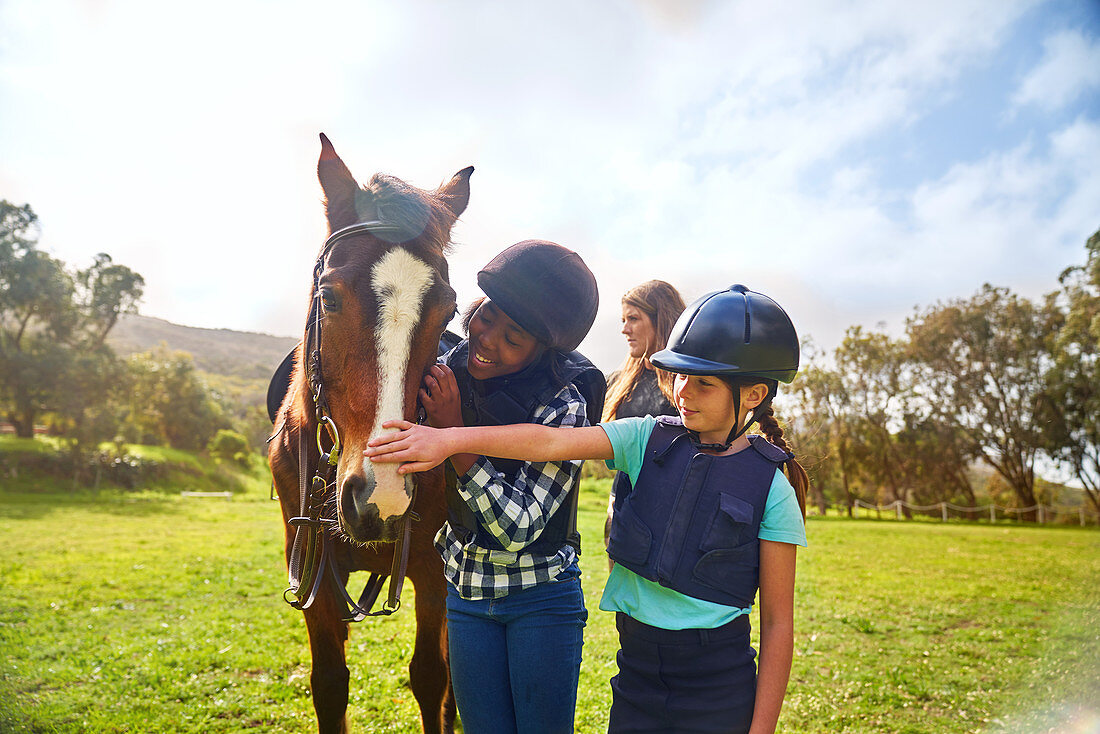 Happy girls petting horse in sunny rural paddock