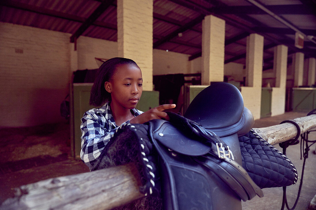 Girl preparing saddle for horseback riding outside stables