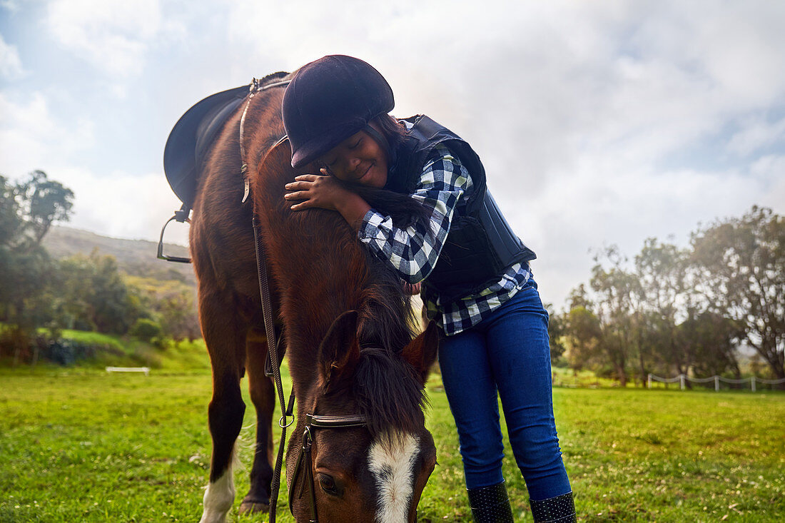 Happy girl hugging horse in rural grass paddock