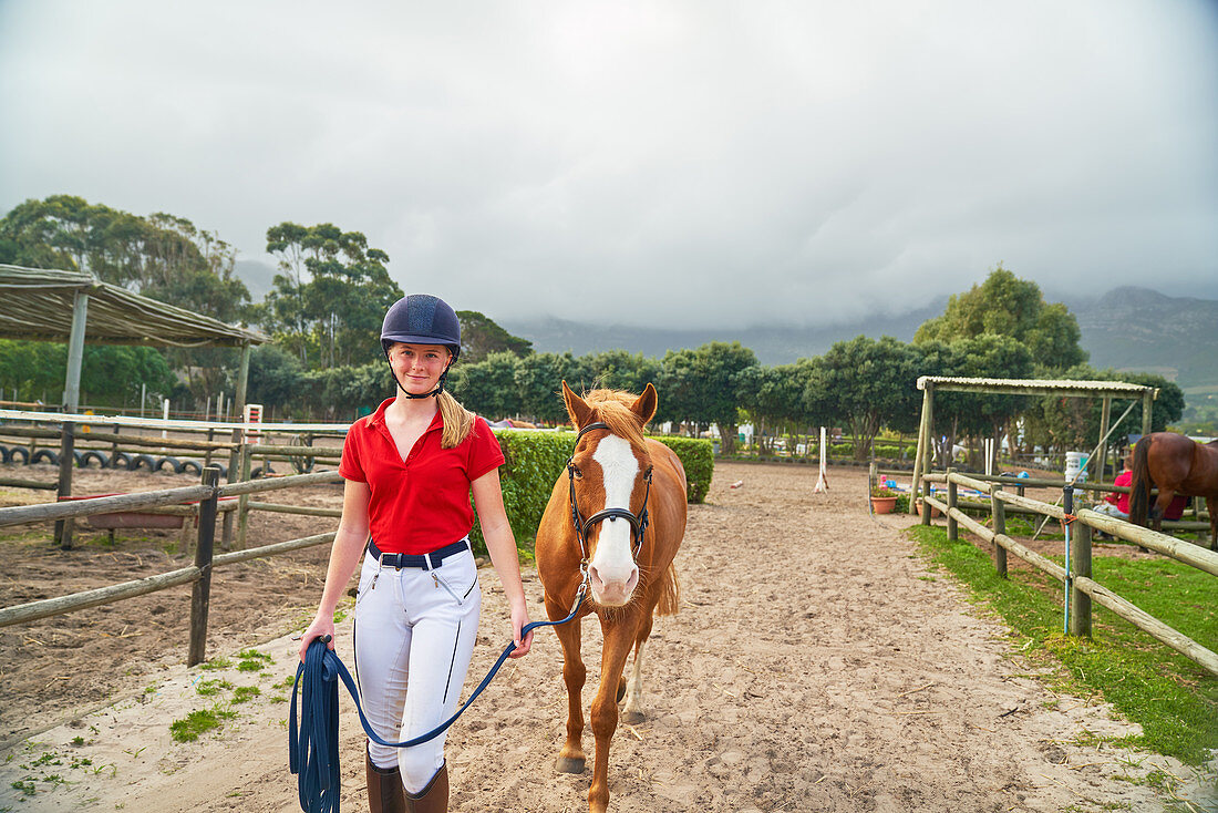 Portrait teenage girl leading horse along rural paddocks
