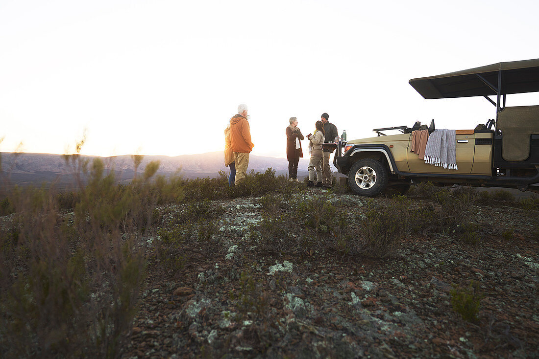 Group drinking tea outside off-road vehicle at sunrise