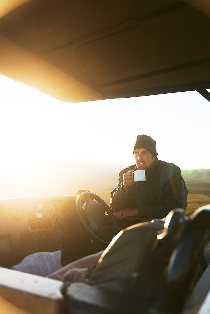 Guide drinking tea at off-road vehicle at sunrise