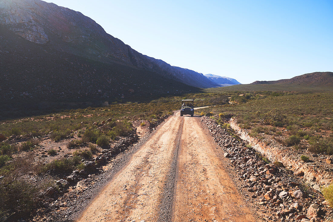 Safari vehicle driving on sunny remote dirt road