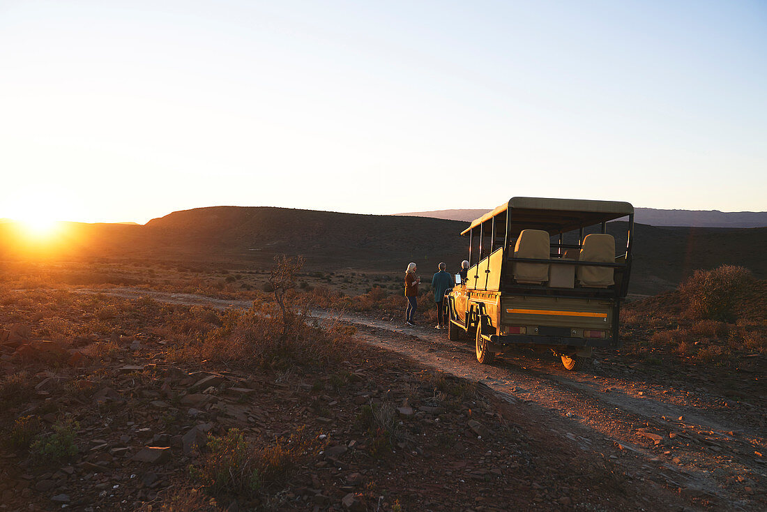 Safari vehicle and tourists at sunset roadside