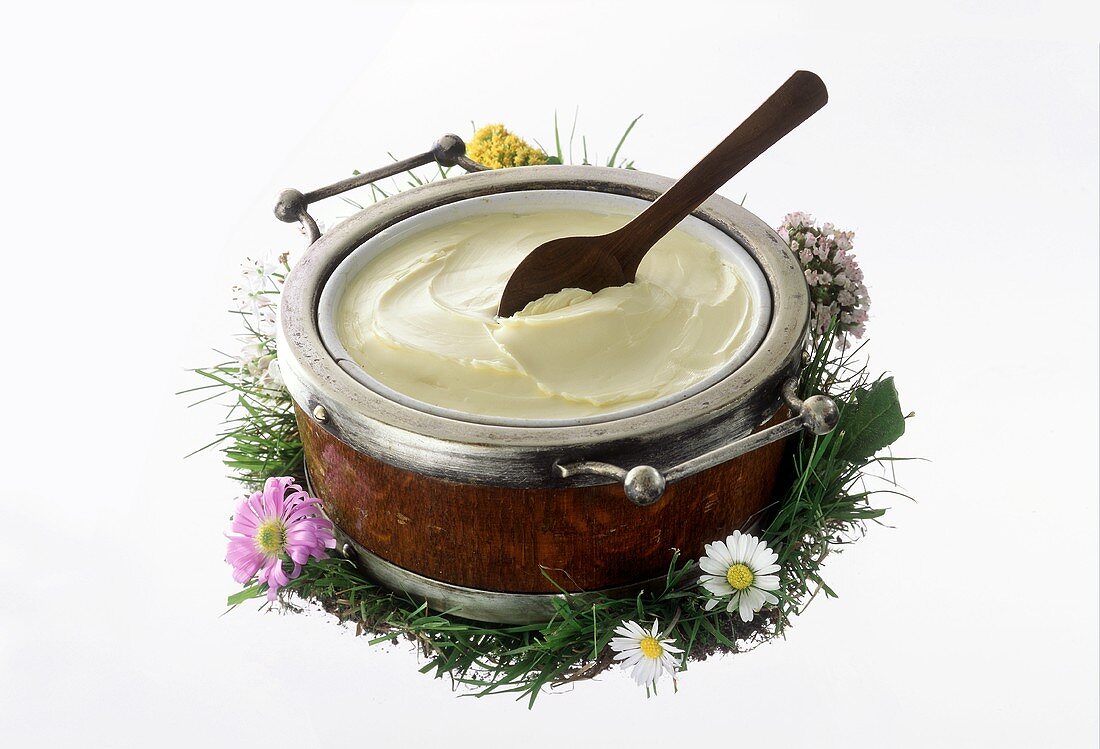 Butter with wooden spoon in pot, on grass with flowers