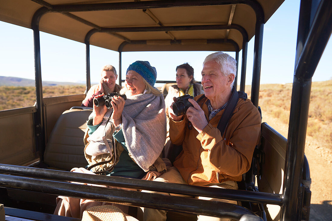 Seniors with binoculars and camera on safari in vehicle