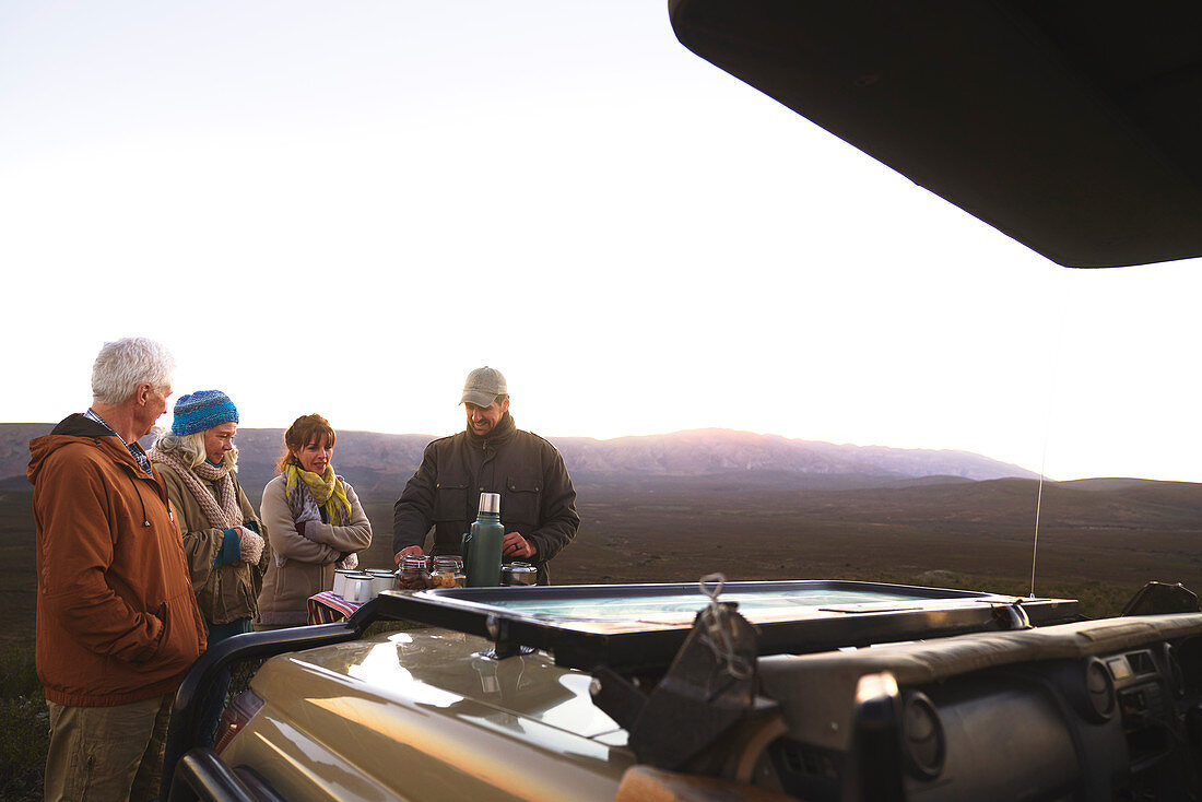 Guide and group enjoying coffee outside off-road vehicle