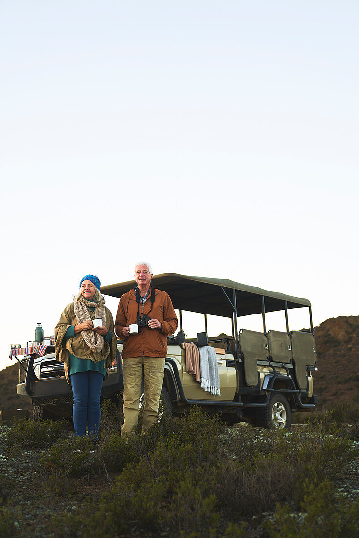 Senior couple on safari drinking tea outside vehicle